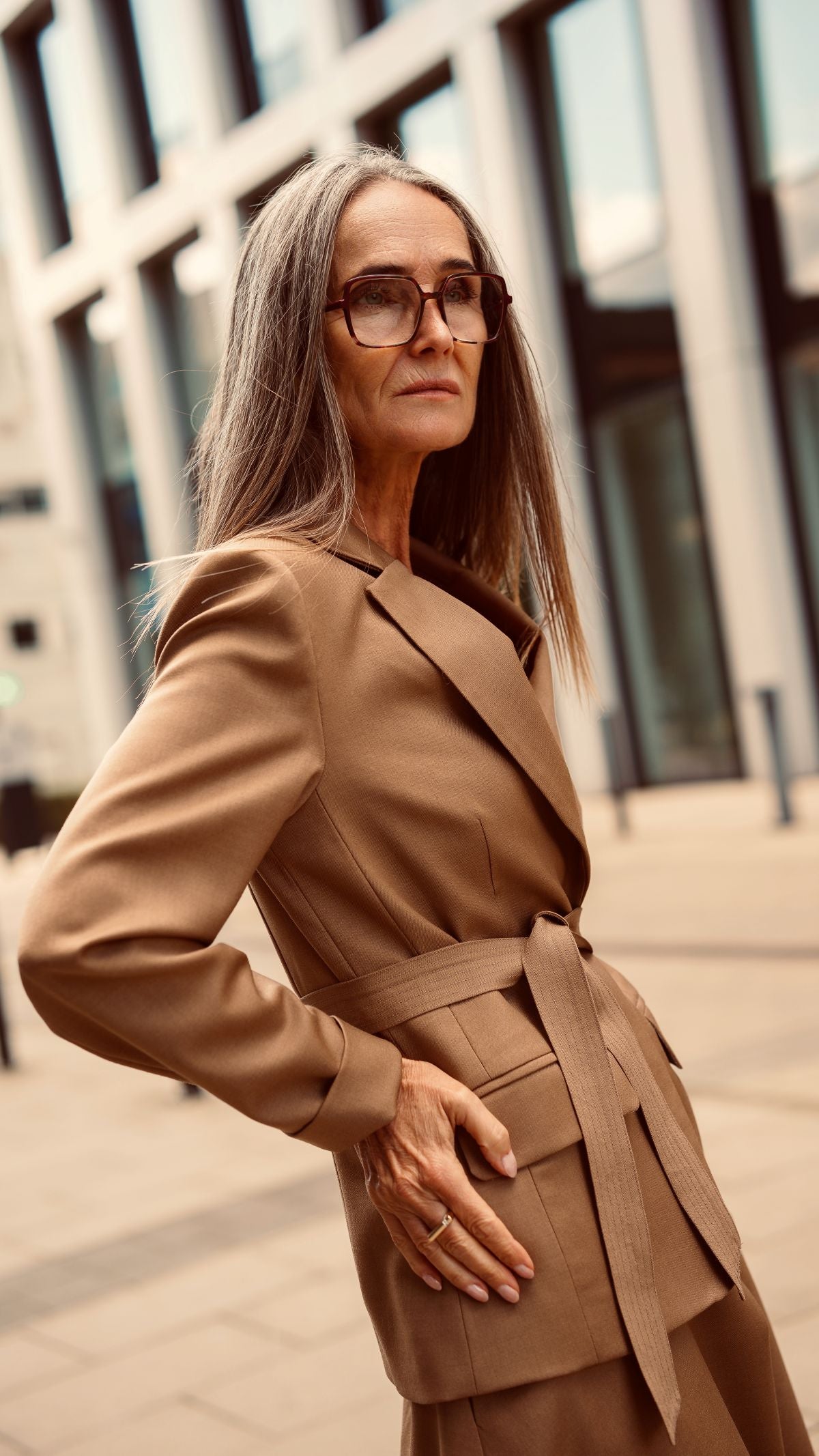 Modelka stoi oparta o ścianę i ma na sobie marynarkę z paskiem jak z kimona