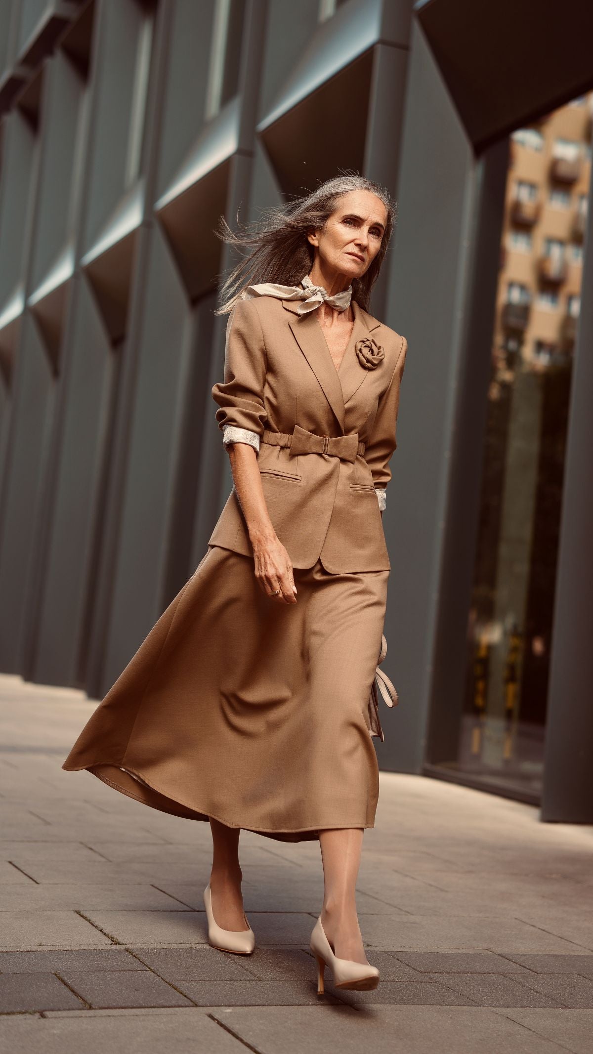 Modelka w wełnianym garniturze damskim w kolorze Taupe idzie ulicą, sylwetka przodem